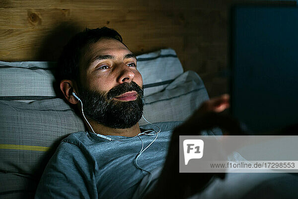 Junger Mann surft nachts im Internet mit Tablet im Bett