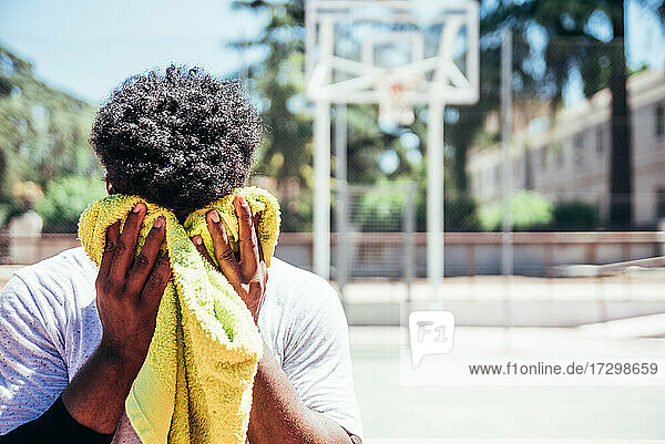 Porträt eines schwarzen afroamerikanischen Jungen  der sich auf einem städtischen Basketballplatz mit einem Handtuch den Schweiß von der Stirn trocknet.