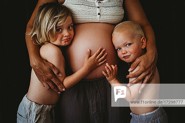 Junge Jungen berühren Mamas schwangeren großen Bauch und schauen in die Kamera