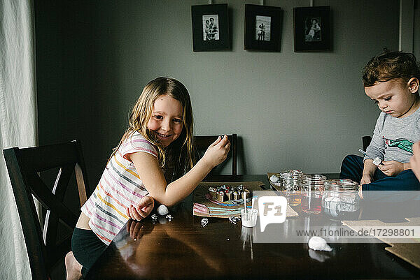 Mädchen lächelnd bei einem Kunstprojekt am Tisch mit ihren Geschwistern