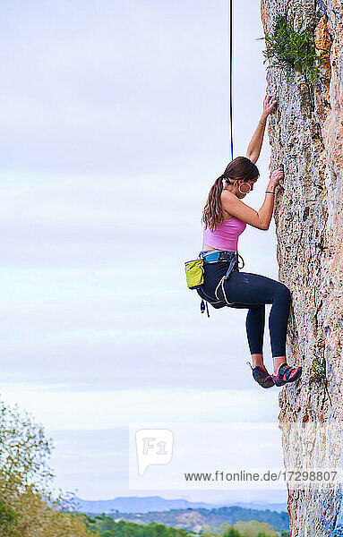 Vertikales Profilfoto einer jungen Frau  die eine steile Felswand erklimmt