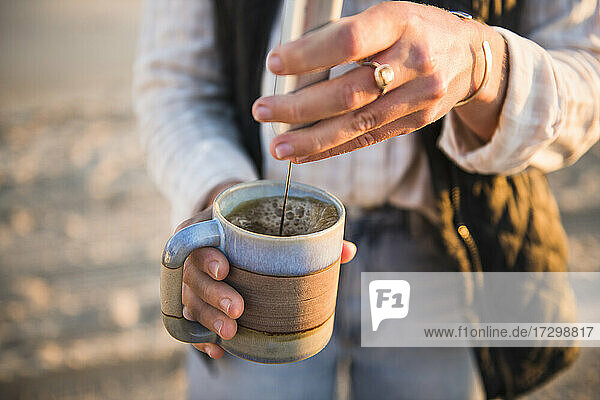 Junge Frau emulgiert Kaffee beim Camping am Strand