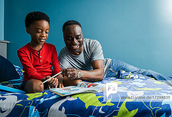 Lächelnder Vater hilft lächelndem Sohn bei den Hausaufgaben auf dem Bett zu Hause
