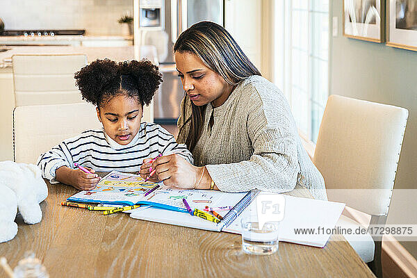 Mother teaching daughter in drawing on book while sitting at table