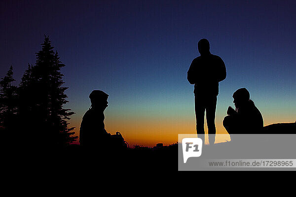 Eine Gruppe von drei Personen genießt einen Abend beim Zelten in den Bergen