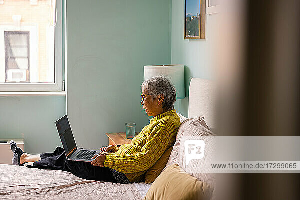 Ältere Frau benutzt einen Laptop  während sie im Schlafzimmer zu Hause sitzt