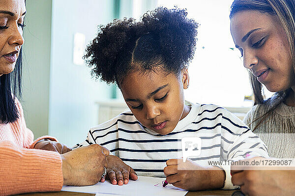 Mutter und Großmutter helfen einem Mädchen beim Zeichnen mit Buntstiften auf Papier zu Hause