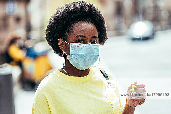 Porträt eines schwarzen Mädchens mit Gesichtsmaske und Afro-Haar  das in einer Straße in der Altstadt wartet.