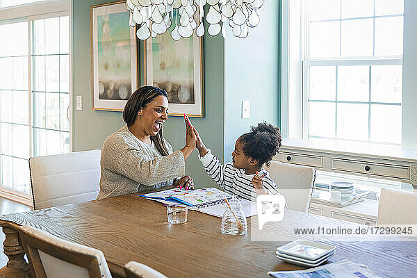 Daughter high-fiving with mother while drawing at table in living room