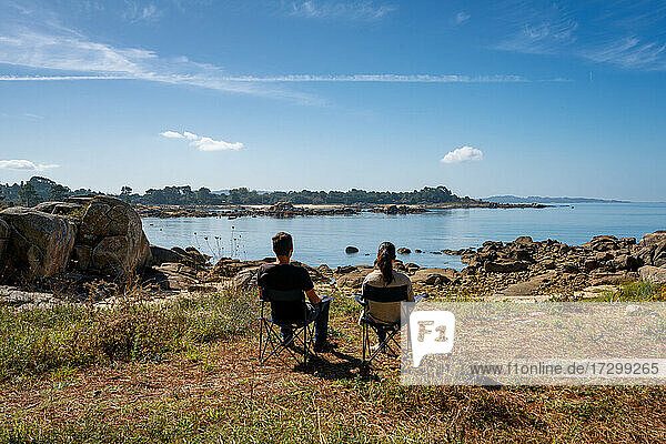 Couple sit on chairs on a wild paradise beach in Arousa island