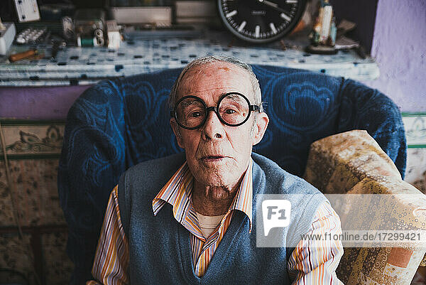 Porträt eines alten Mannes mit Brille  der zu Hause auf dem Sofa sitzt.