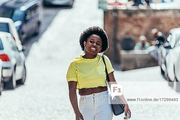 Schwarzes Mädchen mit Afro-Haar  das fröhlich eine Straße in der Stadt entlang läuft.