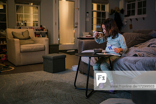 Girl sitting on couch eating cereal early morning