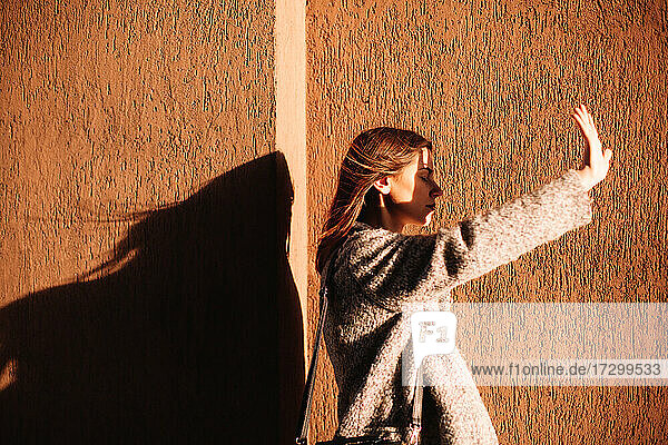 Junge Frau  die ihre Augen gegen die Sonne abschirmt  vor einer Mauer in der Stadt