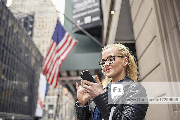 Cheerful woman using smartphone on urban city street