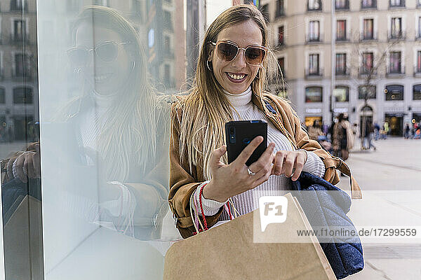 Fröhliche Frau beim Einkaufen in der Stadt. Sie benutzt ihr Smartphone.