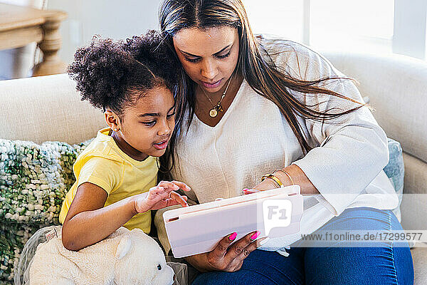 Mutter und Tochter benutzen ein digitales Tablet  während sie zu Hause auf dem Sofa sitzen