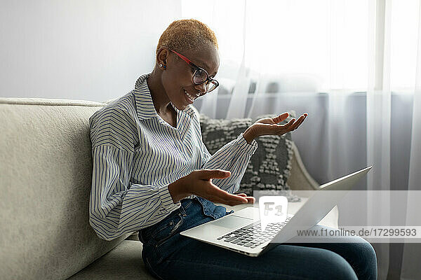 Lächelnde schwarze Frau  die zu Hause über ihren Laptop ein Online-Meeting abhält