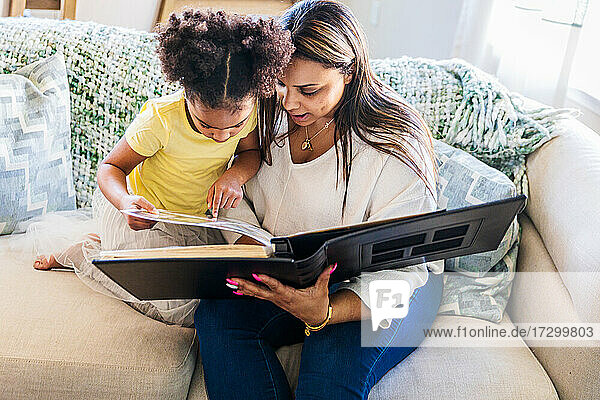Mutter und Tochter betrachten ein Fotoalbum  während sie zu Hause auf dem Sofa sitzen