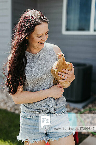 Frau hält Huhn in ihrem Garten an einem sonnigen Tag