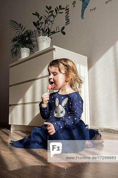 das Mädchen sitzt auf dem Boden und isst Süßigkeiten am Stiel