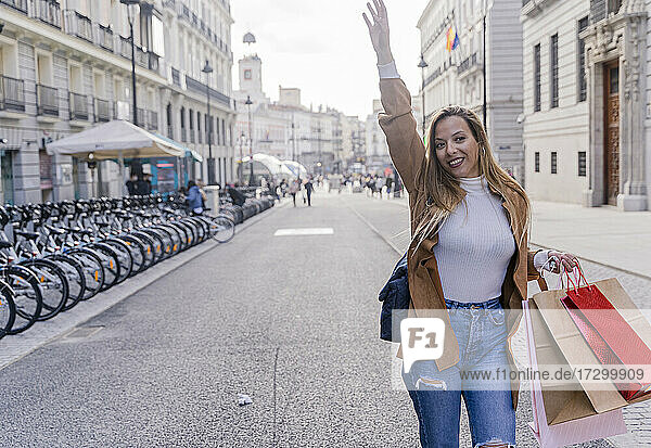 Lächelnde junge Touristin  die im Freien auf ein Taxi wartet. Fröhliche moderne Dame mit Tasche gestikuliert  um dem Taxifahrer ein Signal zu geben. Taxi-Service-Konzept