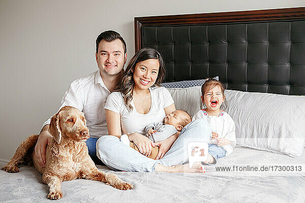 Happy multiracial young family with kids and dog pet on bed at home.