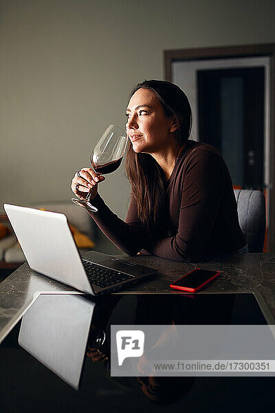 Brünette Frau trinkt Wein und benutzt einen Laptop