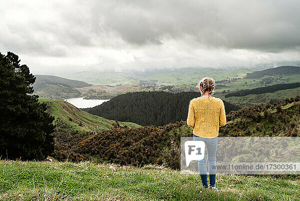 Tween girl in yellow sweater looking at lake from hillside in New Zealand