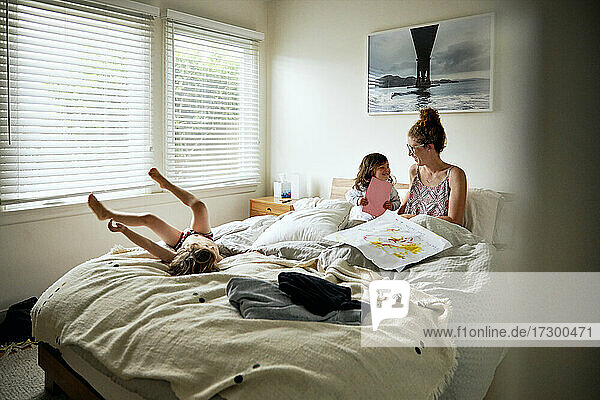 Daughter giving greeting card to mother on bed at home