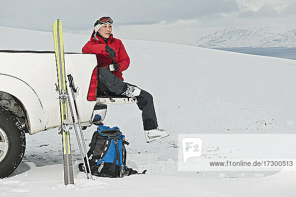 Frau sitzt auf der Rückseite eines Pick-ups und macht eine Pause vom Skifahren