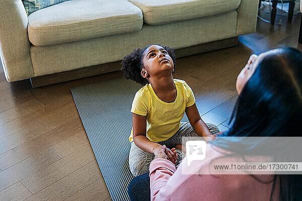 Mädchen übt mit ihrer Großmutter Yoga  während sie auf einer Übungsmatte im Wohnzimmer sitzt