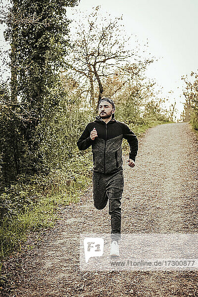 Man in cap and dark tracksuit running through the forest