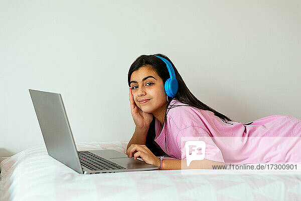 Fröhlicher Teenager  der im Bett einen Laptop benutzt und Musik hört