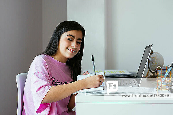 Fröhlicher Teenager beim Lernen am Schreibtisch im eigenen Zimmer