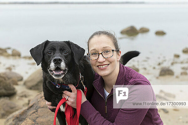 Close-up portrait smiling woman with old black lab at Cape Cod beach