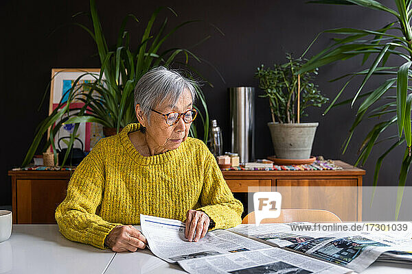 Ältere Frau im gelben Pullover liest zu Hause Zeitung