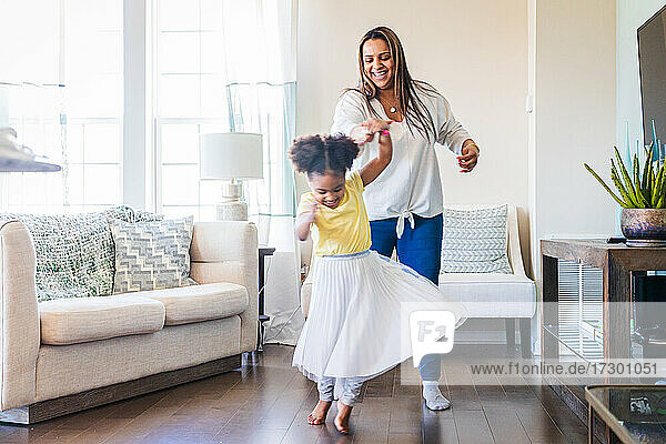 Glückliche Mutter hält die Hand ihrer Tochter  die im Wohnzimmer zu Hause Tanz übt