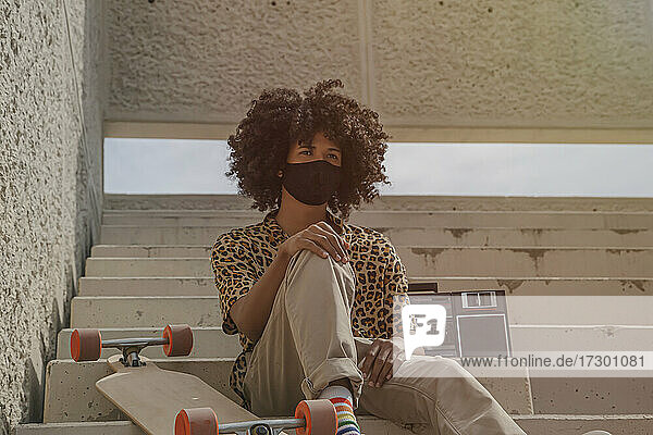 Young afro man with mask sitting on some stairs with a longborad