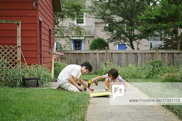 Ein Sohn und ein Vater bauen zusammen mit einer elektrischen Bohrmaschine im Hinterhof