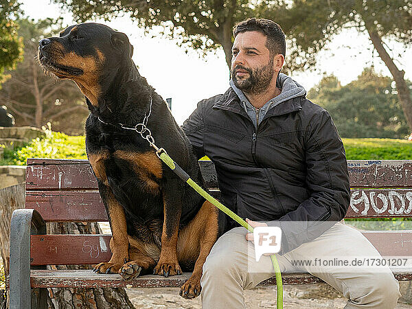 Mann sitzt auf einer Parkbank neben seinem Rottweiler-Hund