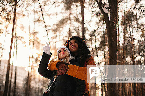 Young woman embracing her girlfriend standing in park in winter