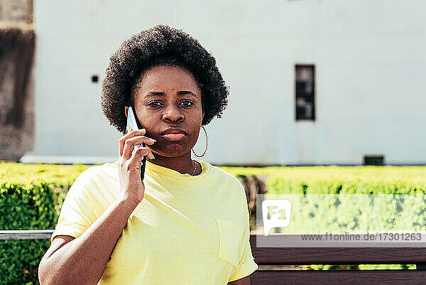 Porträt eines schwarzen Mädchens mit Afro-Haar und Ohrringen  das in einer städtischen Umgebung telefoniert.