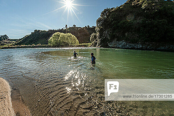 Preteen children walking in New Zealand river on sunny day
