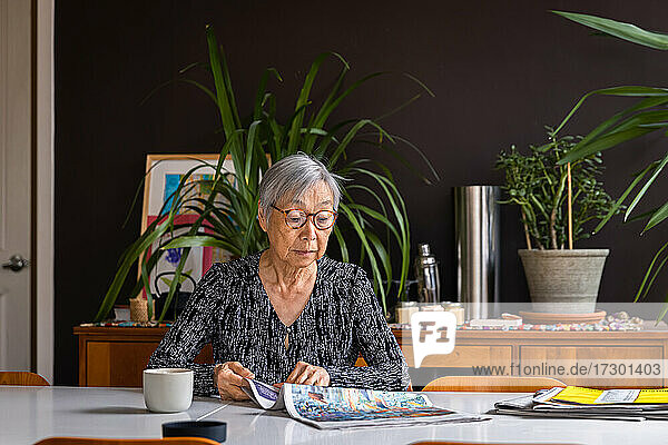 Senior woman reading newspaper while sitting at table with coffee