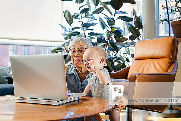Ältere Frau sitzt mit ihrer Enkelin zusammen und benutzt einen Laptop für einen Videoanruf