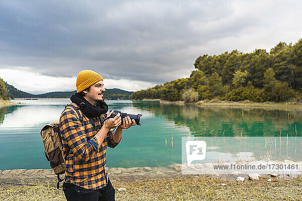 Smiling tourist taking pictures with his camera in nature