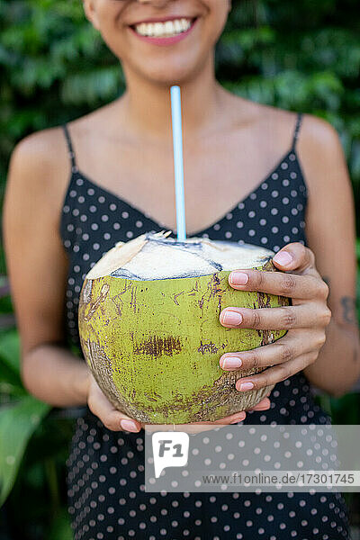 Junge Frau hält lächelnd eine frische Kokosnuss