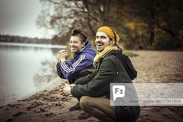 two happy queer friends sit by lake in winter laughing and chatting