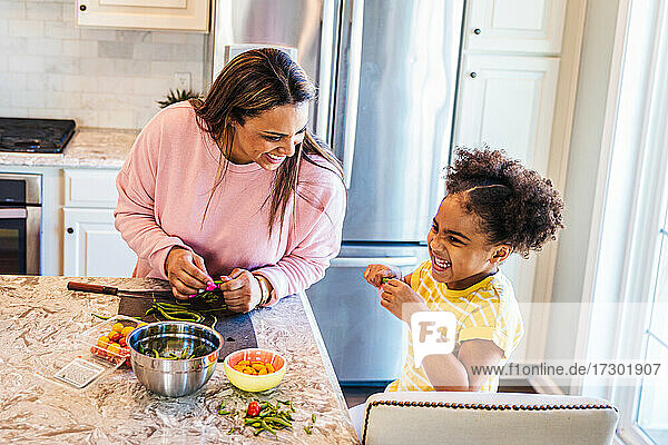 Lächelnde Tochter hilft Mutter bei der Zubereitung von Essen in der Küche zu Hause